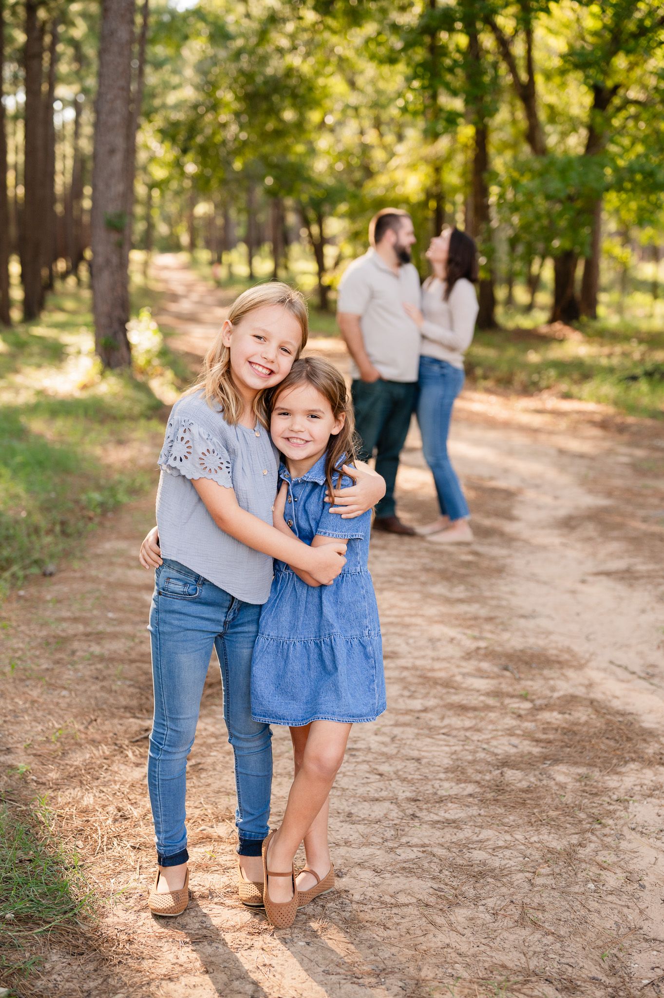 A family enjoys a sunny afternoon walk together on a dirt path through a wooded forest area on a warm day.