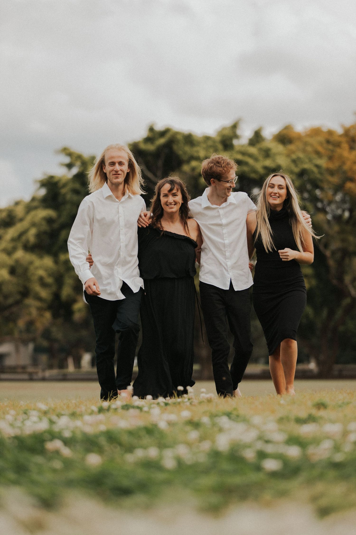 A group of four people wearing black and white outfits laughing while walking together outdoors on a cloudy day.