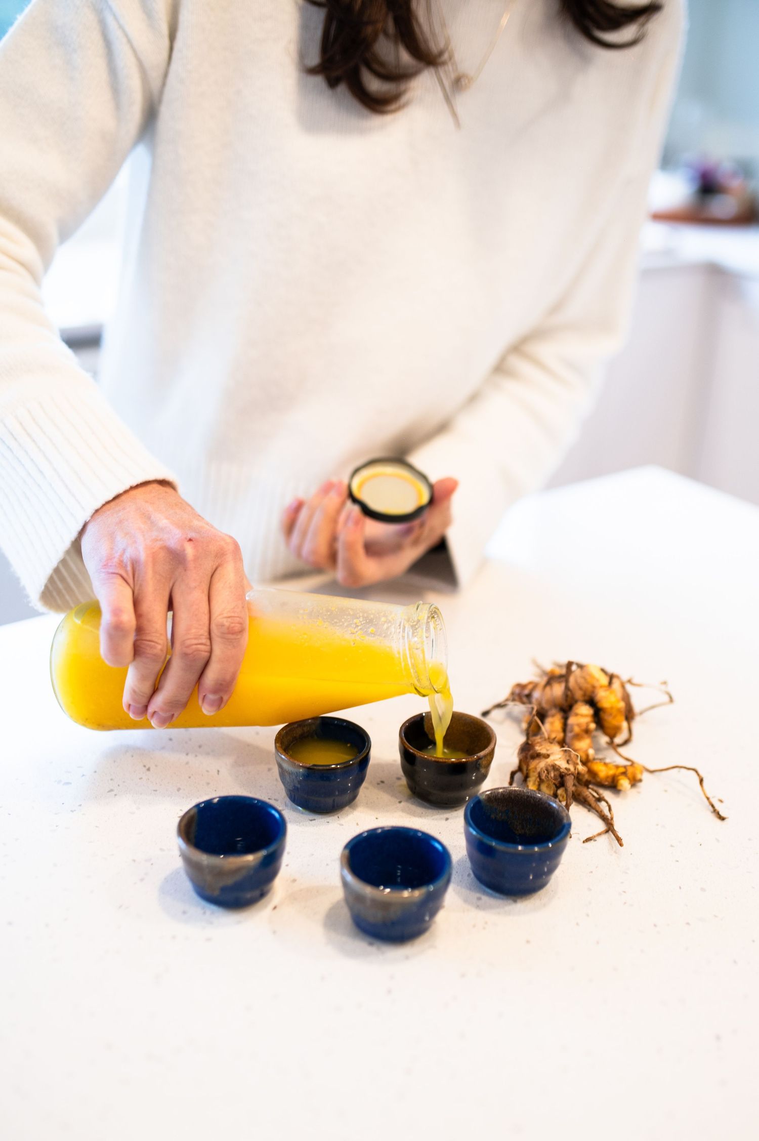 Orange juice being poured into blue ceramic cups on white surface with ginger root nearby.