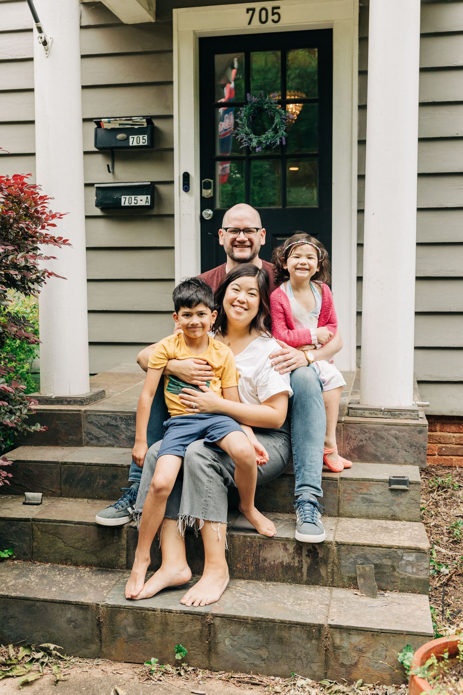 A family sits together smiling on the front steps of house with a wreath on the door in Charlotte, NC