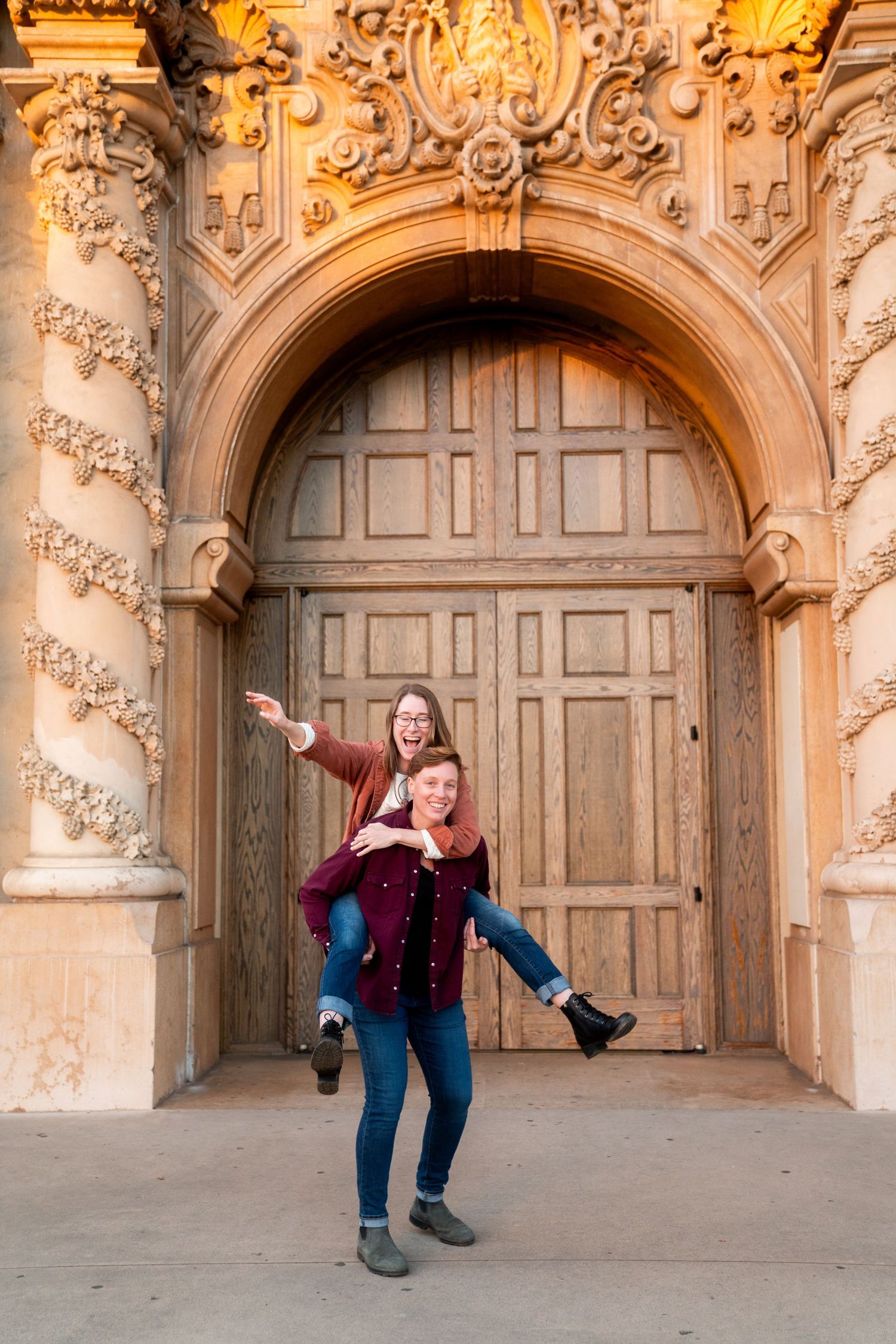 A playful couple poses in front of an ornate archway with decorative stonework during a photo session.