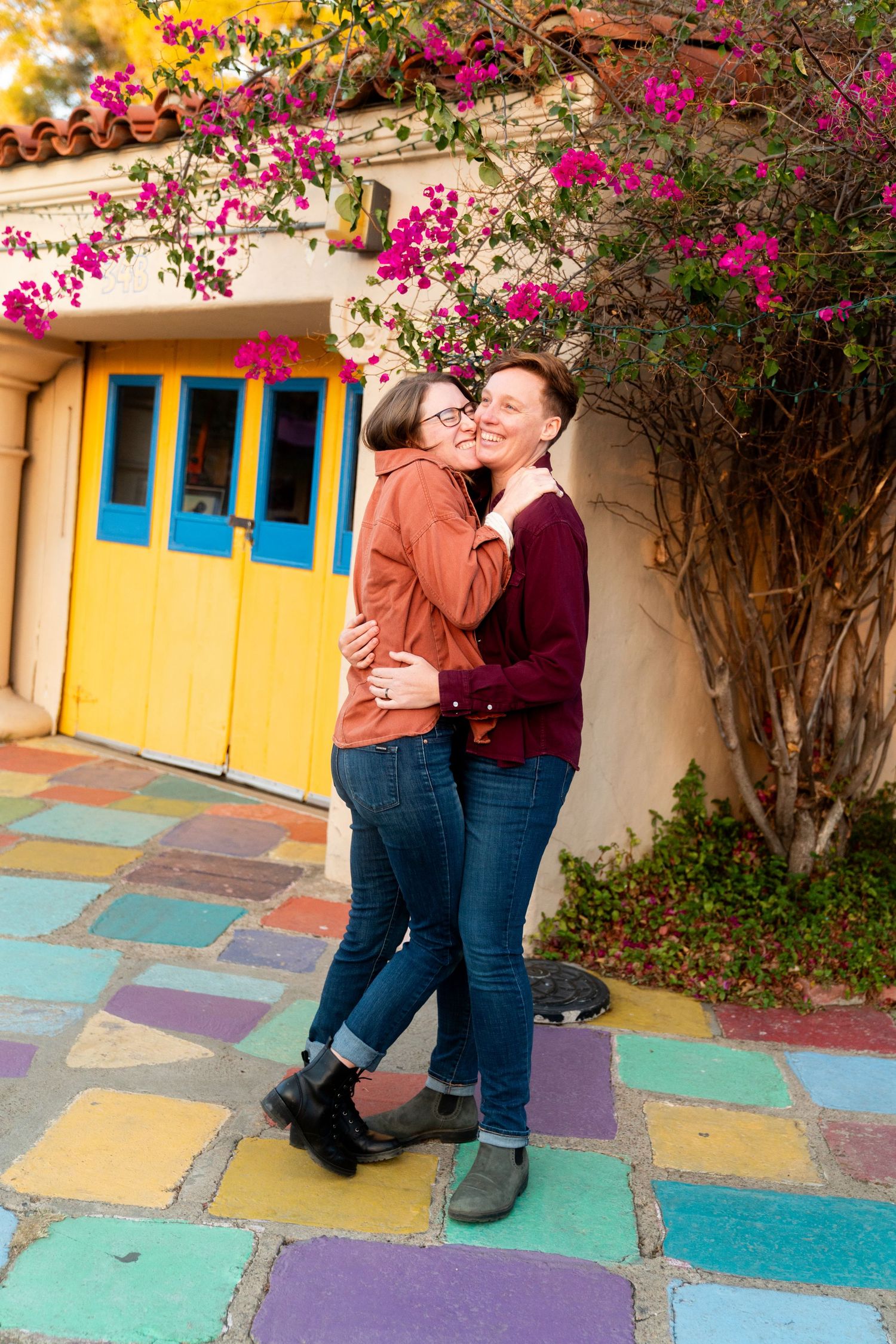 A romantic moment shared on a colorful tiled patio with bright pink bougainvillea and yellow door in the background.