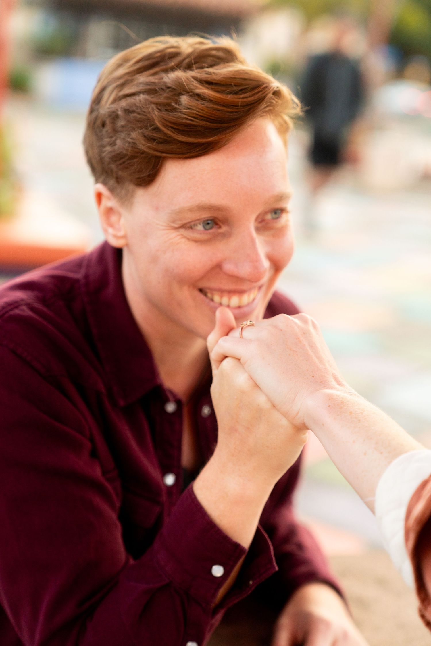 A tender moment captured as someone in a burgundy sweater smiles warmly during an engagement.