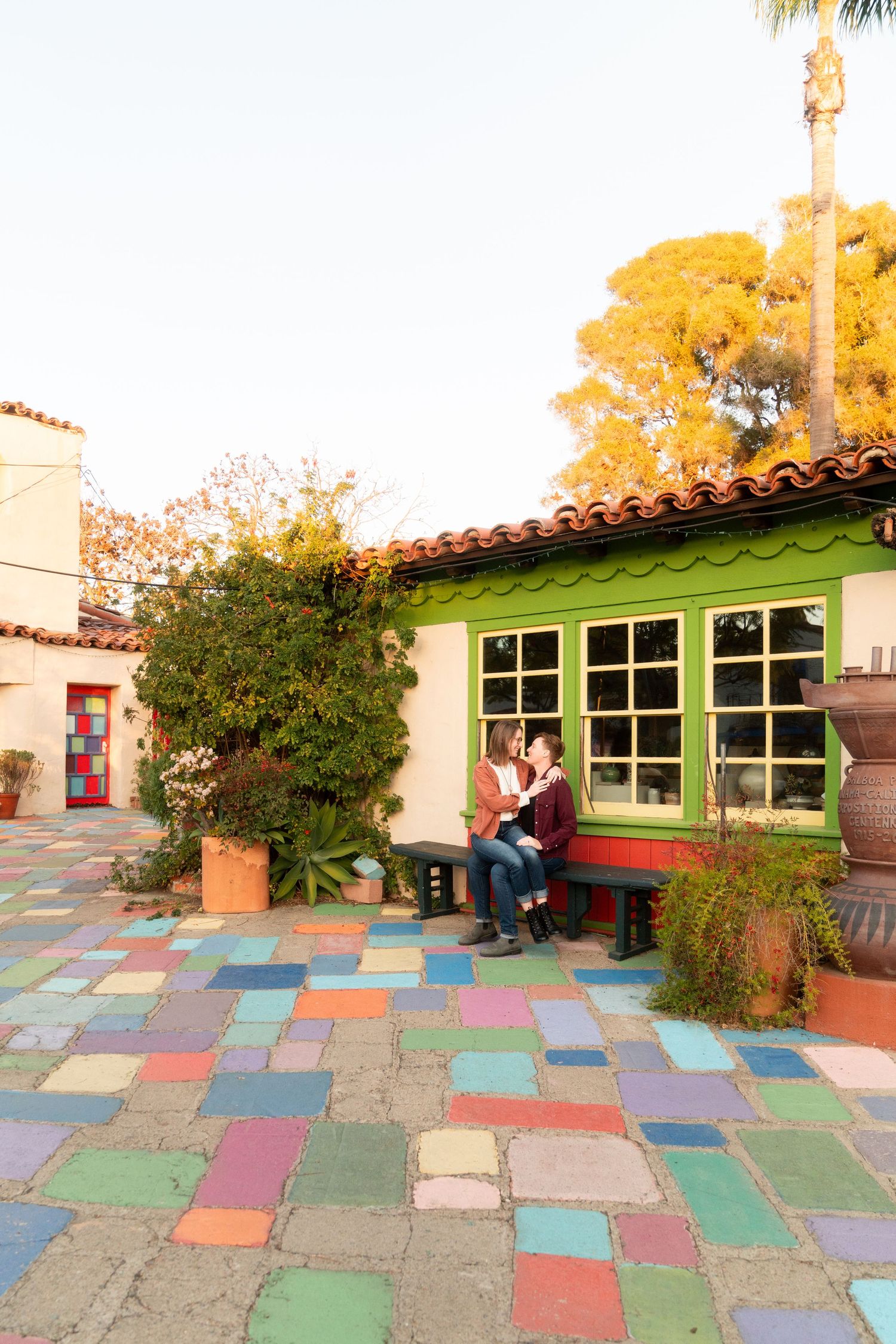 Colorful tiled courtyard with Spanish-style architecture featuring green windows and a bench nestled against a cream building.