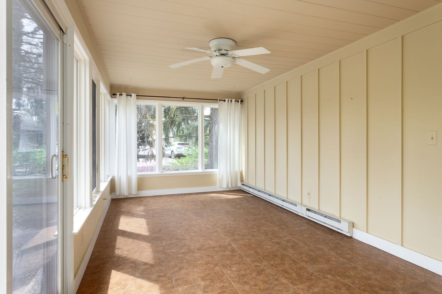 Enclosed sunroom with beige walls, ceiling fan, and cork flooring surrounded by large windows.