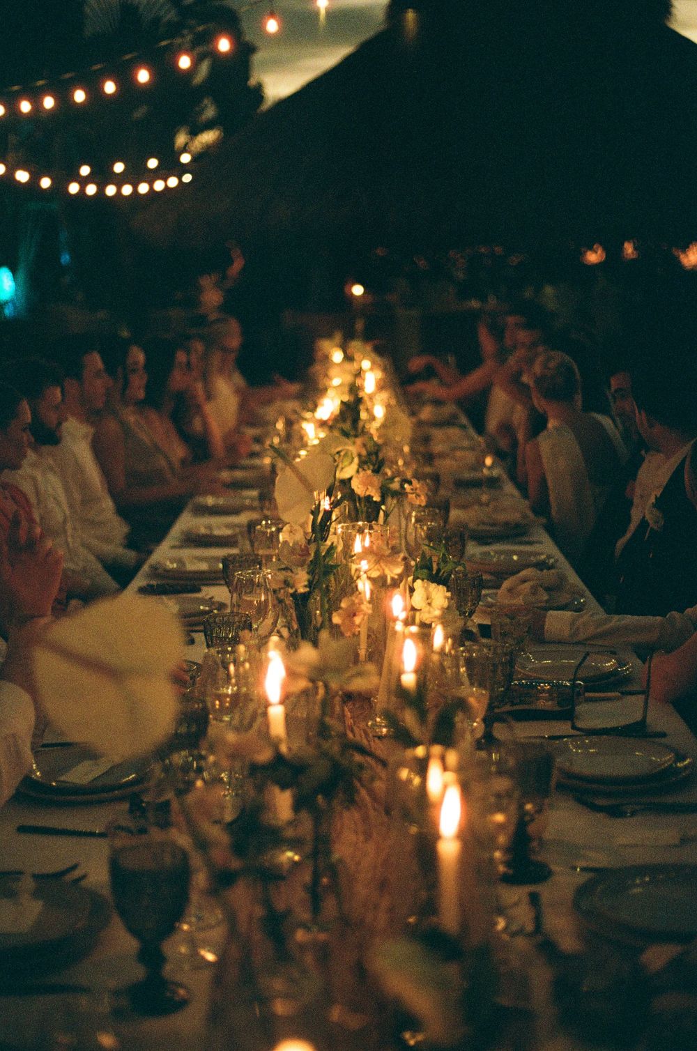 Candlelit dinner table set for an elegant outdoor evening gathering with string lights and moody ambient lighting.