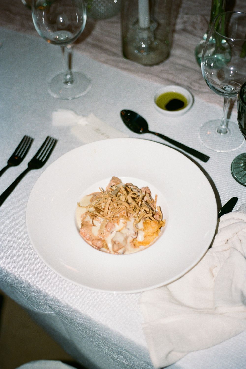 An elegant pasta dish served on a white plate with garnish and utensils at a formal dining setting.