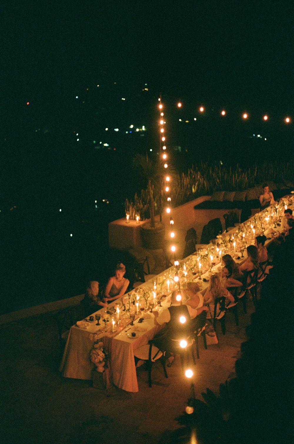 A romantic outdoor dinner setting with string lights illuminating a long table at night.