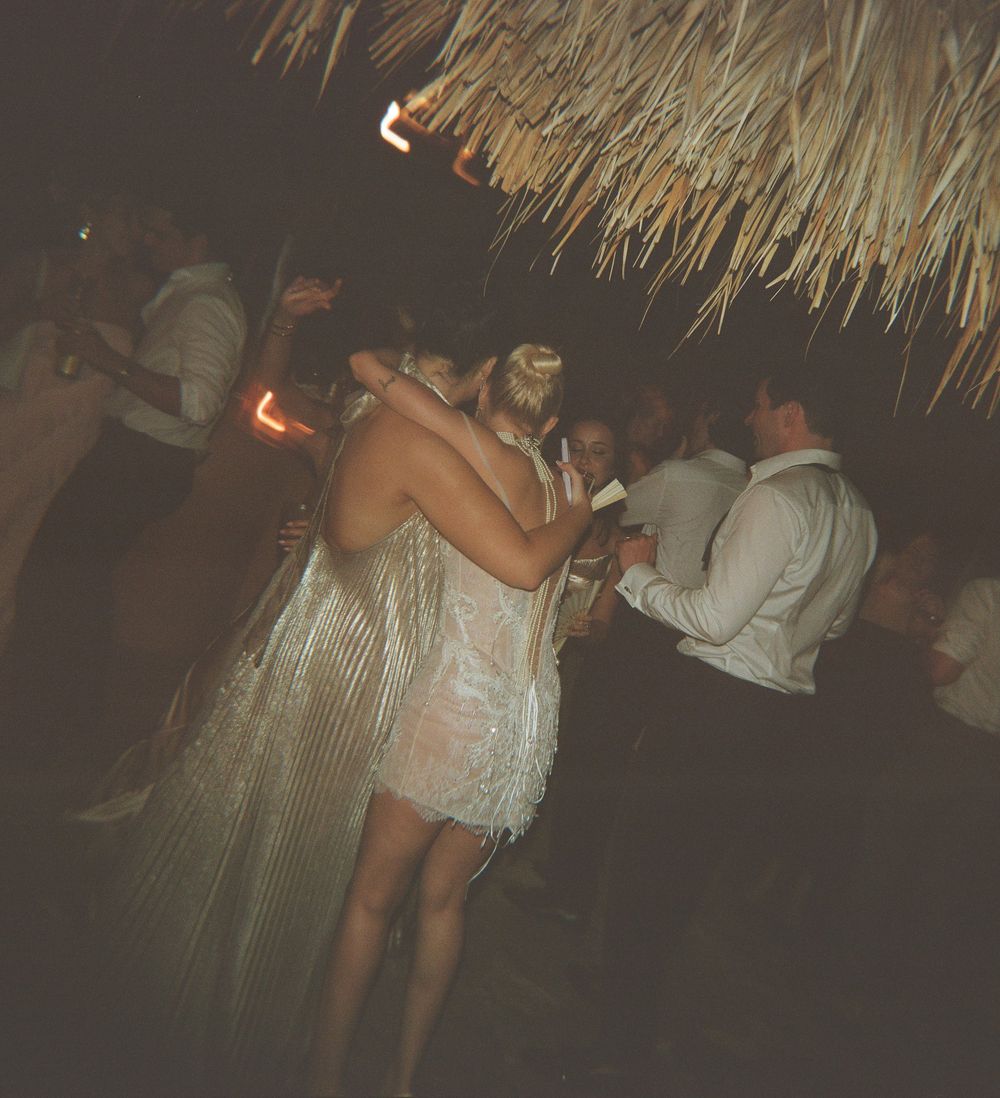 Partygoers dancing under a thatched roof at a nighttime beach celebration.