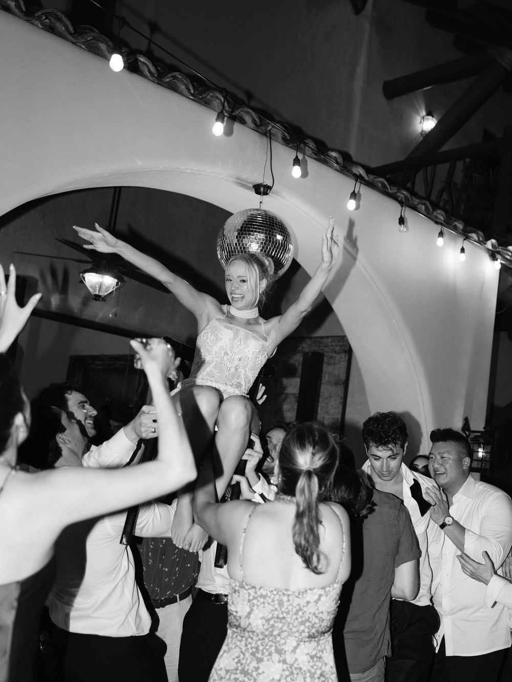 Party guests lifting and celebrating with someone in white dress during festive reception.