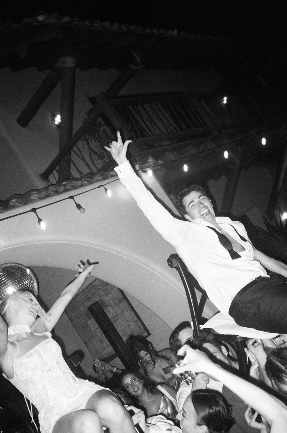 Wedding party guests jumping and celebrating on a dance floor under string lights.