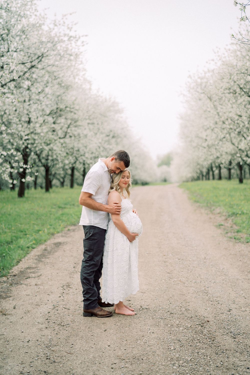 A couple shares a tender moment on a dirt path surrounded by blooming spring trees.