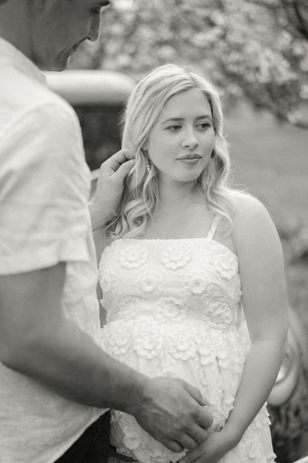 A couple dressed in white embraces among spring blossoms in black and white photography.