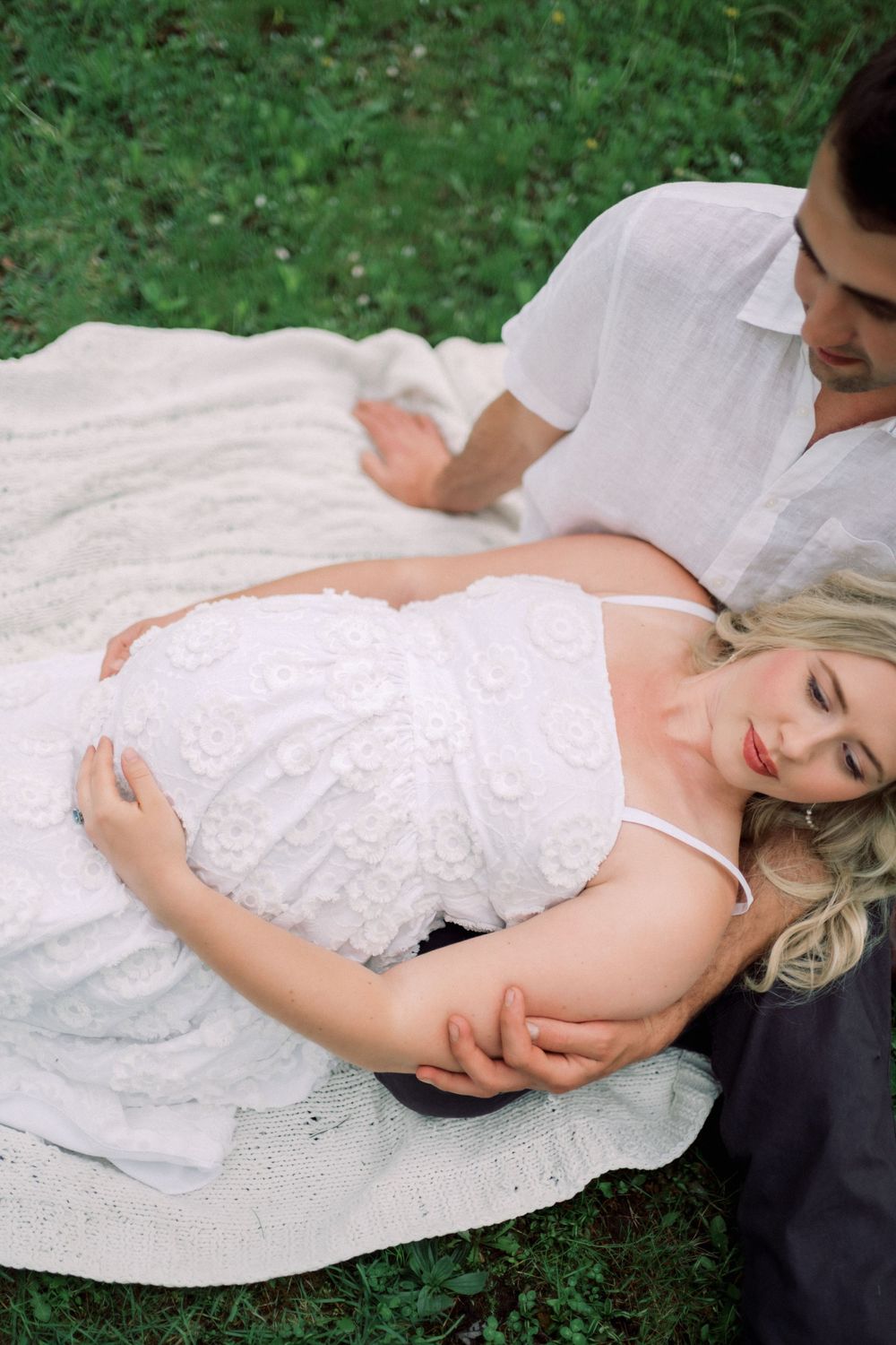 A tender moment captured on a white picnic blanket in a lush green garden setting.