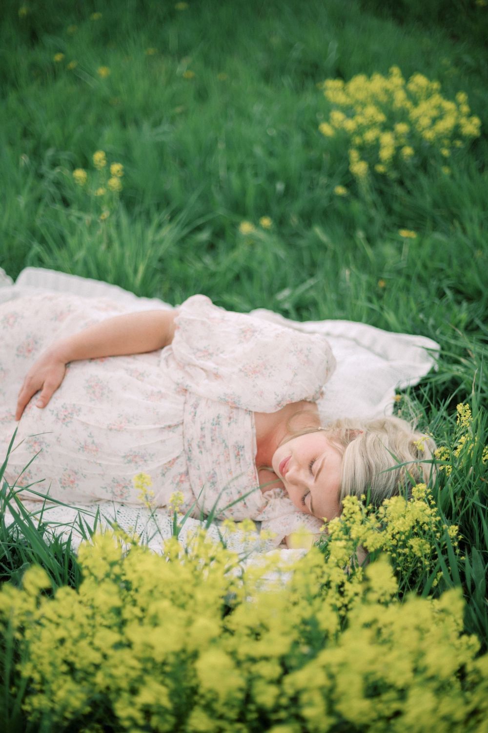A dreamy spring scene with someone resting on a white lace blanket among bright yellow wildflowers and green grass.