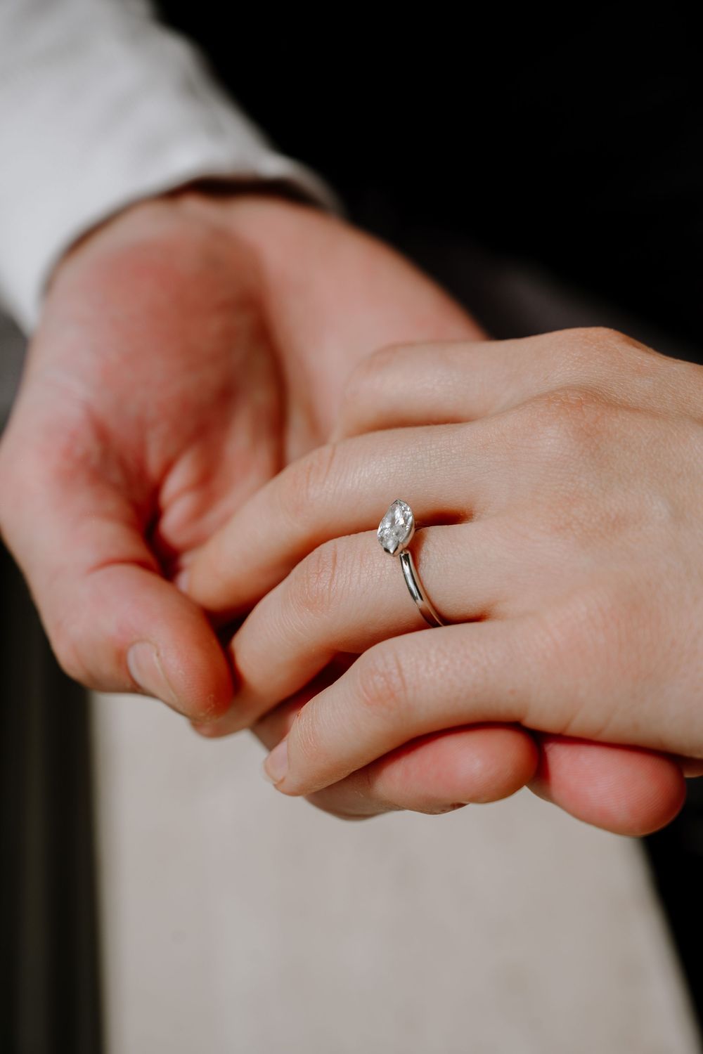 Close-up shot of hands holding each other with a delicate diamond engagement ring on display.