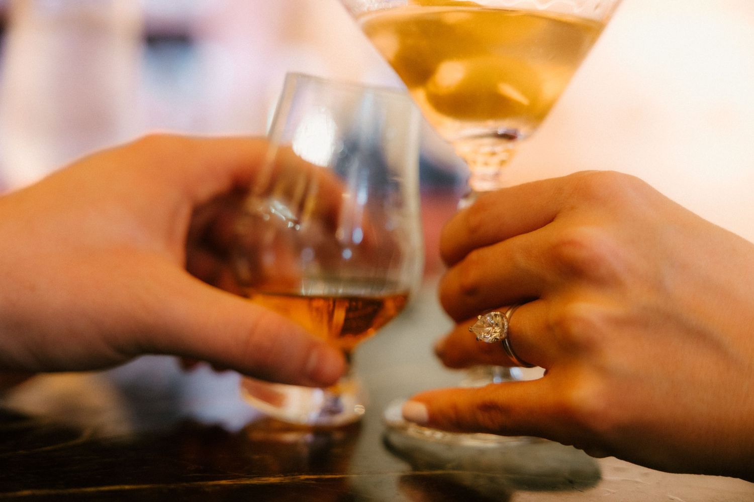 Two hands holding wine glasses with beverages clinking in a celebratory cheers gesture.