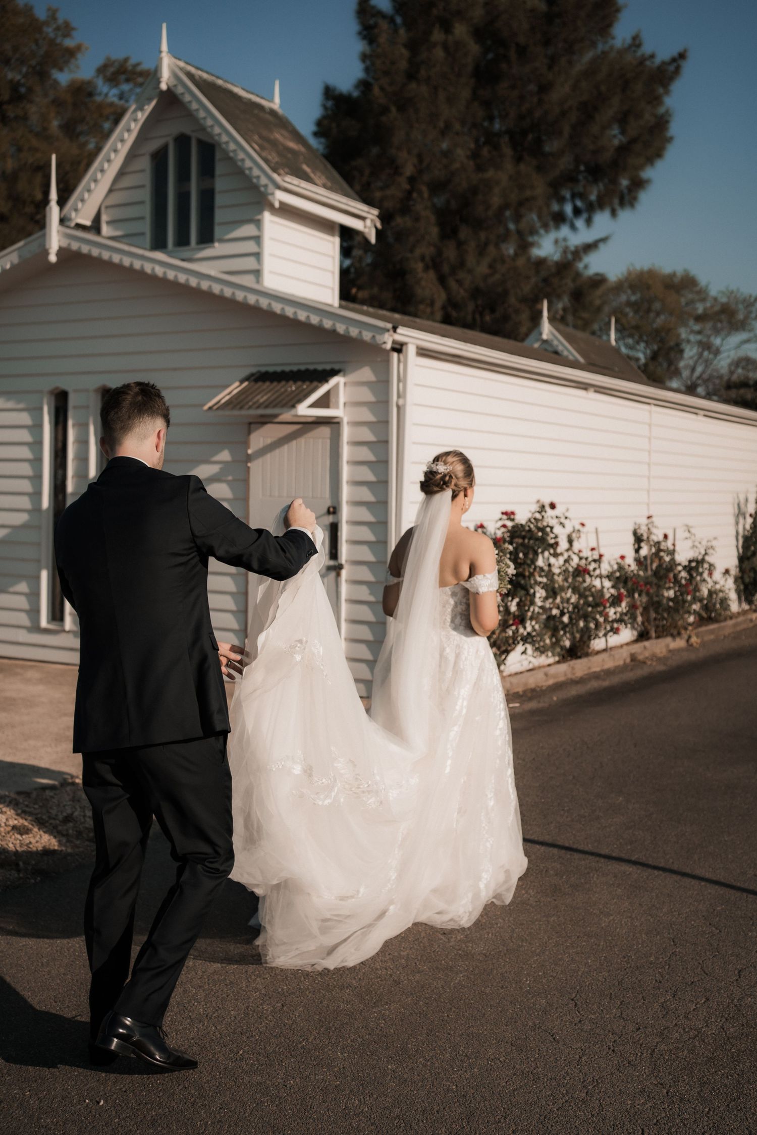 A couple walking near a white chapel building with flowing wedding dress.