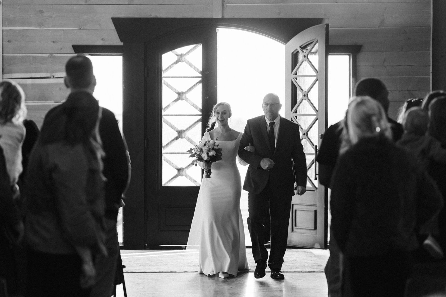 A wedding couple makes their entrance through double doors into a venue while guests look on in this black and white photo.