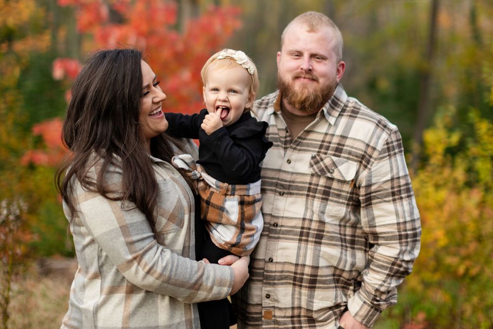 A family of three shares a candid outdoor moment together against vibrant autumn foliage.