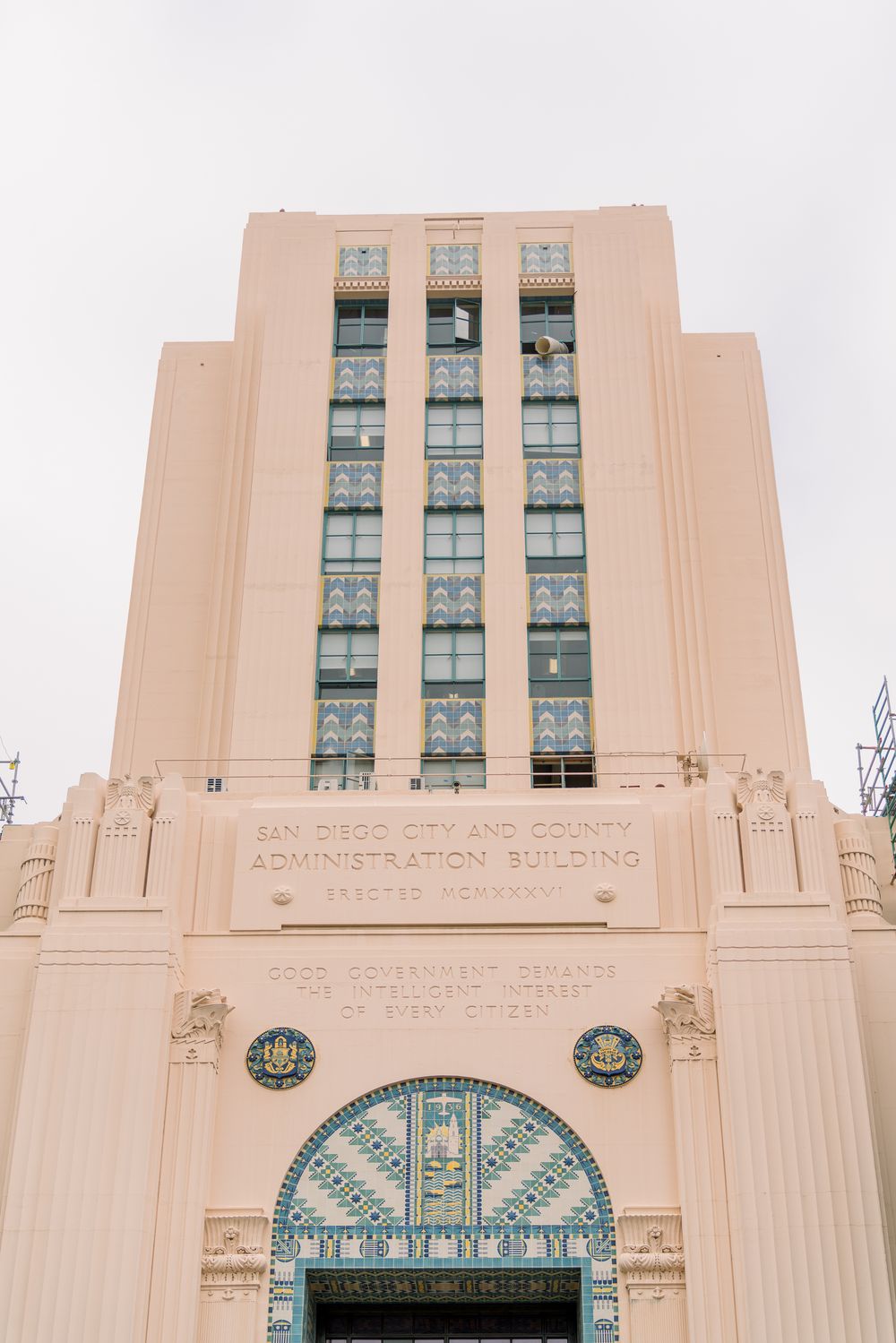 Art deco style beige building facade with ornate turquoise details and vertical window columns.