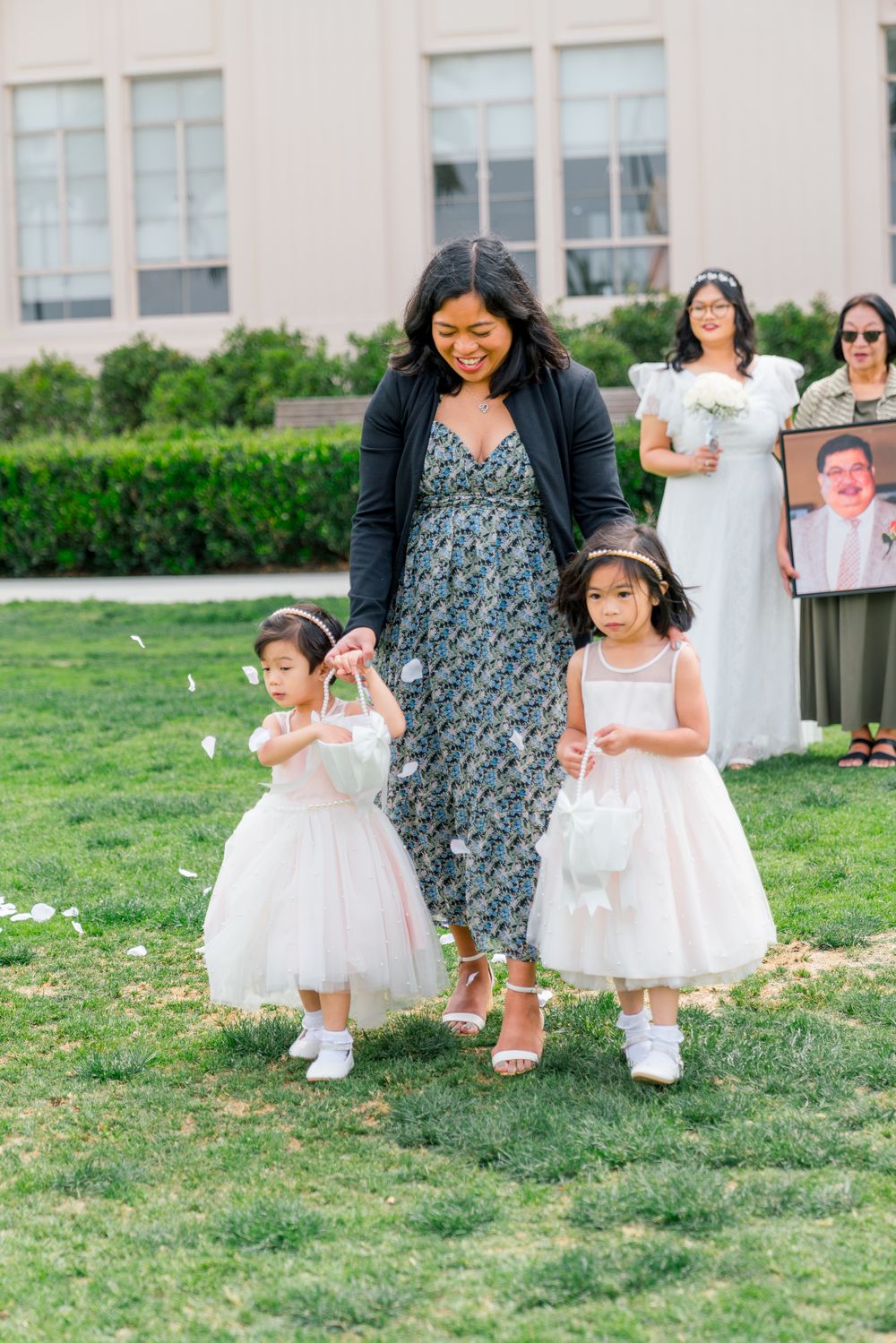 A celebratory outdoor gathering with flower girls in white dresses on a lawn.