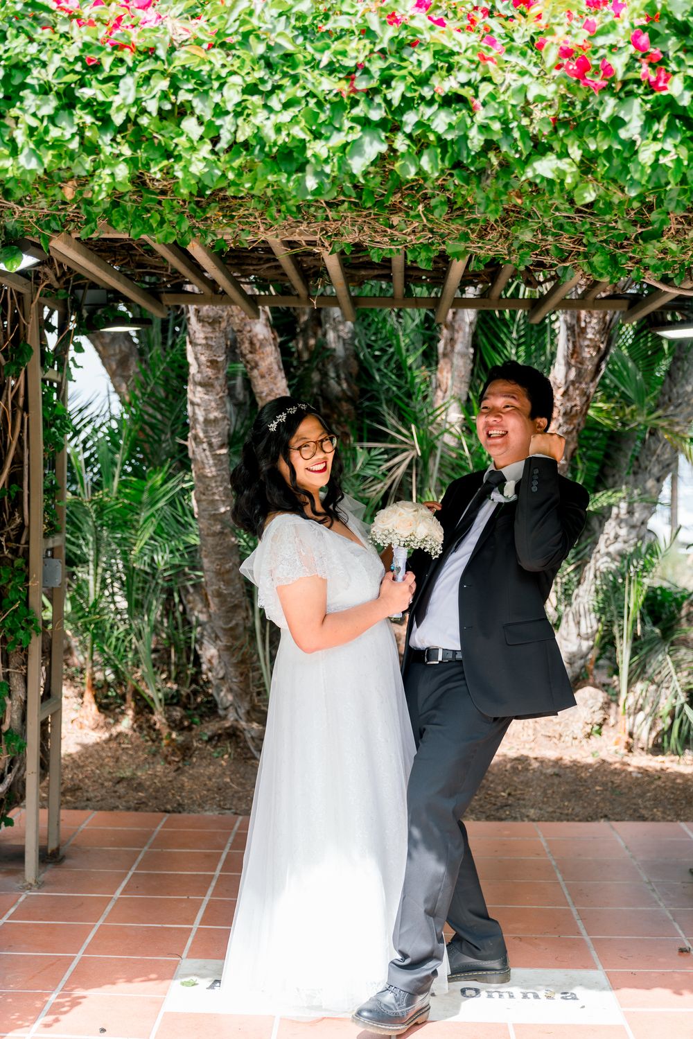 A couple shares a happy moment under a floral-covered pergola during their wedding celebration.