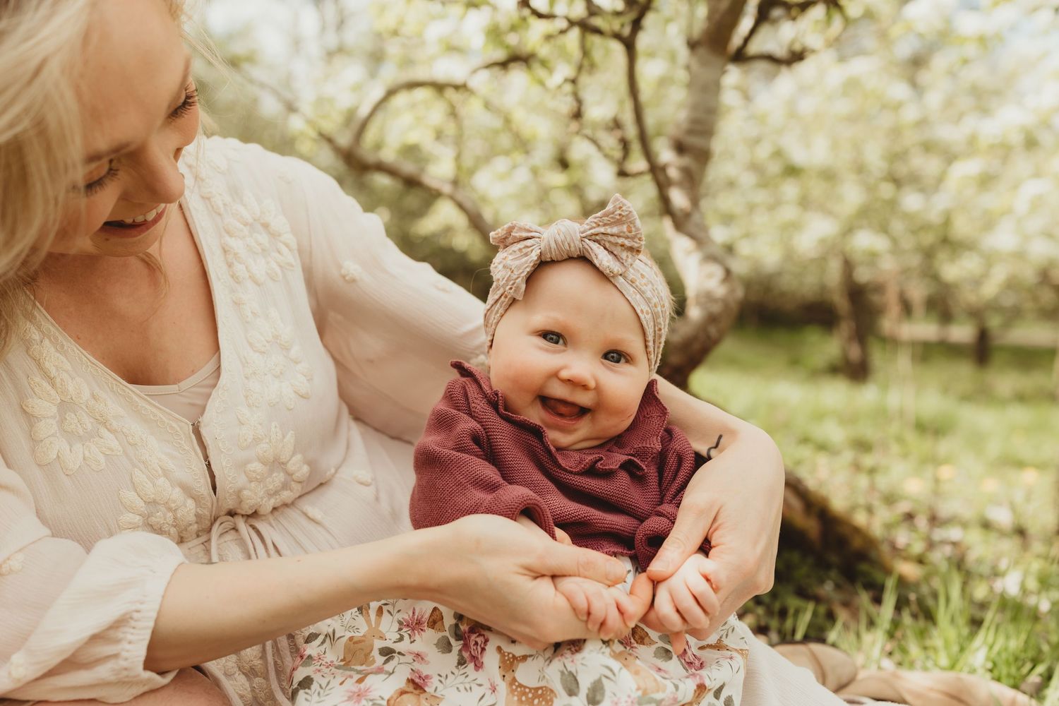 Candid spring photo showing child in burgundy top and headband sitting with someone in white dress outdoors.