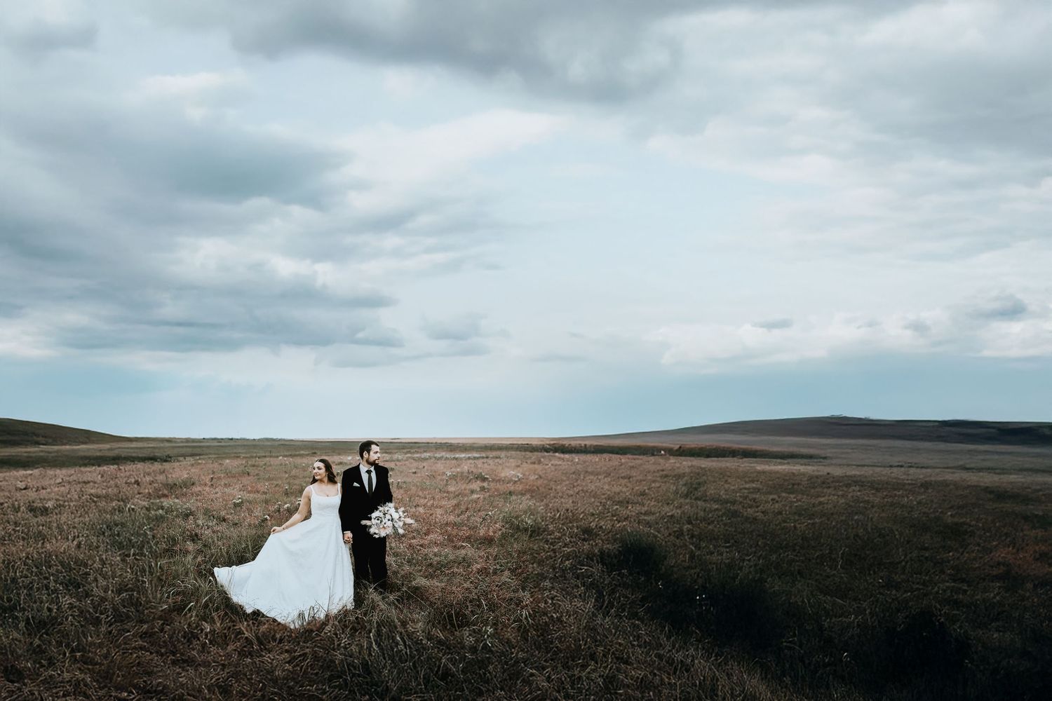 a wide angle photo of a bride and groom standing in a field just before the storm hits at their wedding venue in collinsville, tx