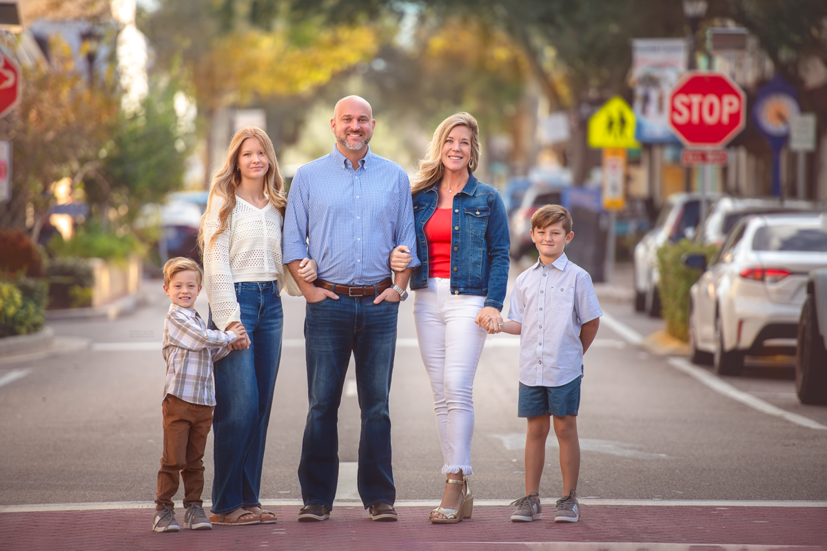 Family portrait taken on street of Downtown Cocoa Beach. Family is holding hands and smile to camera.