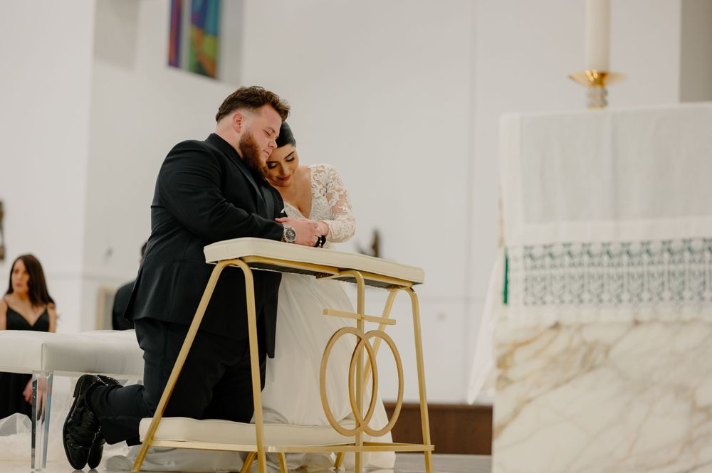 A couple shares an intimate moment at gold and marble decorated table inside an elegant white church during a ceremony.