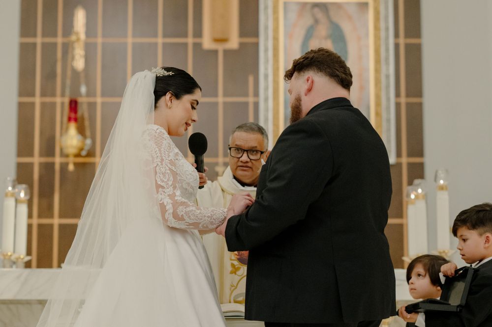 A couple exchanges rings during their wedding ceremony in a church with an ornate altar backdrop.
