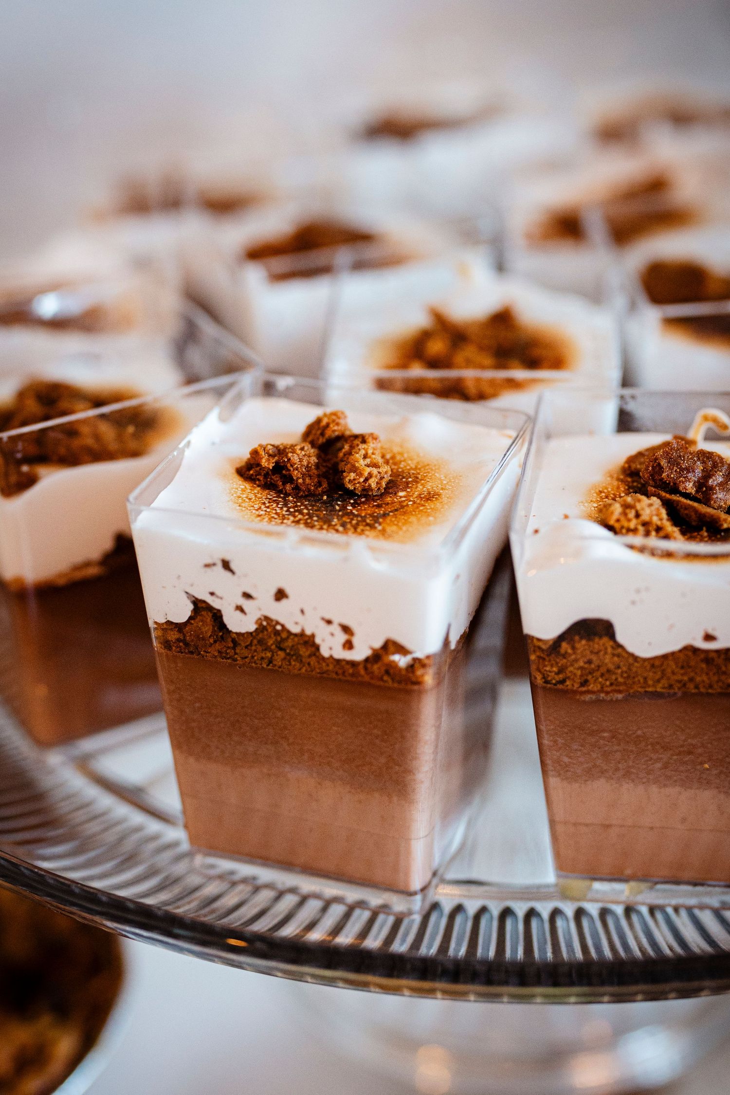 Layered chocolate mousse dessert cups with white cream topping and cookie crumbles served on a glass platter.