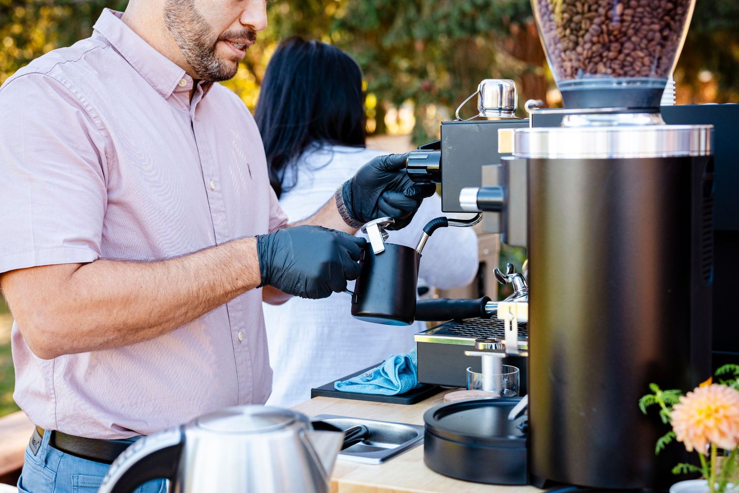 Barista operating a commercial coffee grinder at an outdoor coffee service station.