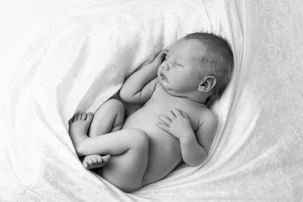 naken nyfødt baby liggende på siden med bena i kryss i et fotostudio for nyfødtbilder i Lyngdal