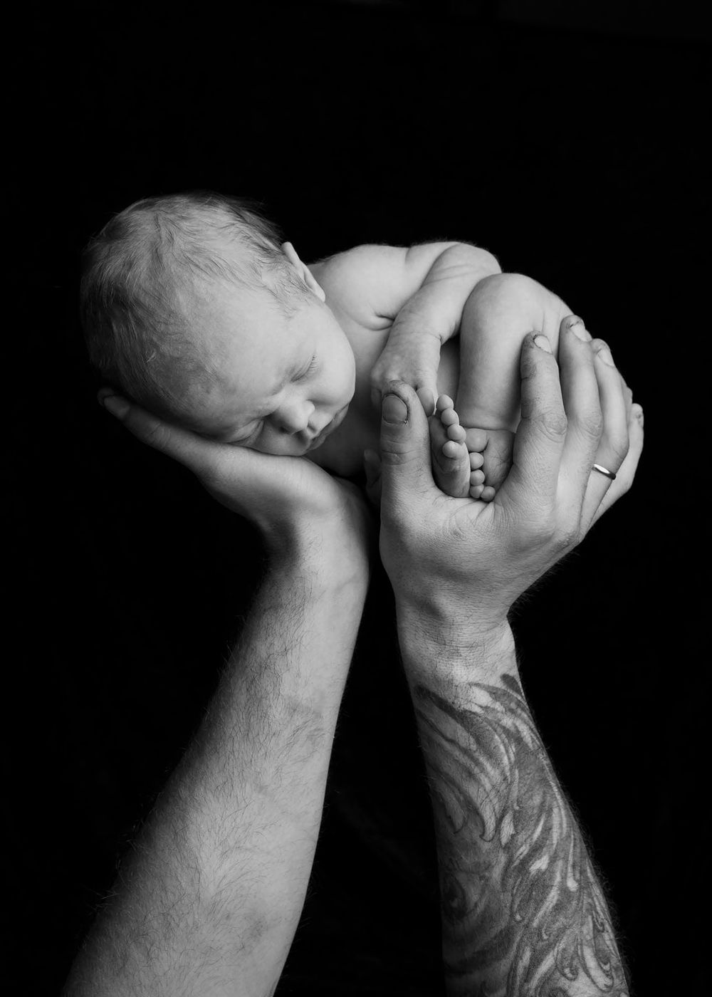 Nyfødtbaby holdes av armene til tatovert pappa på nyfødtfotografering i Lyngdal