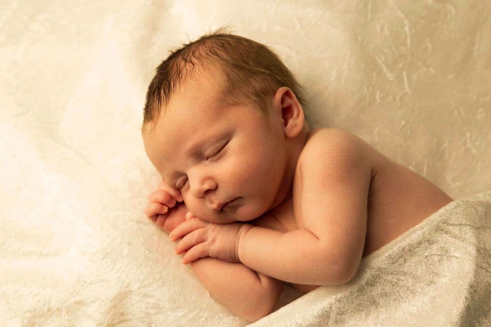 Portrett av Nyfødt baby liggende på hendene sine på siden under nyfødtfotografering i Flekkefjord