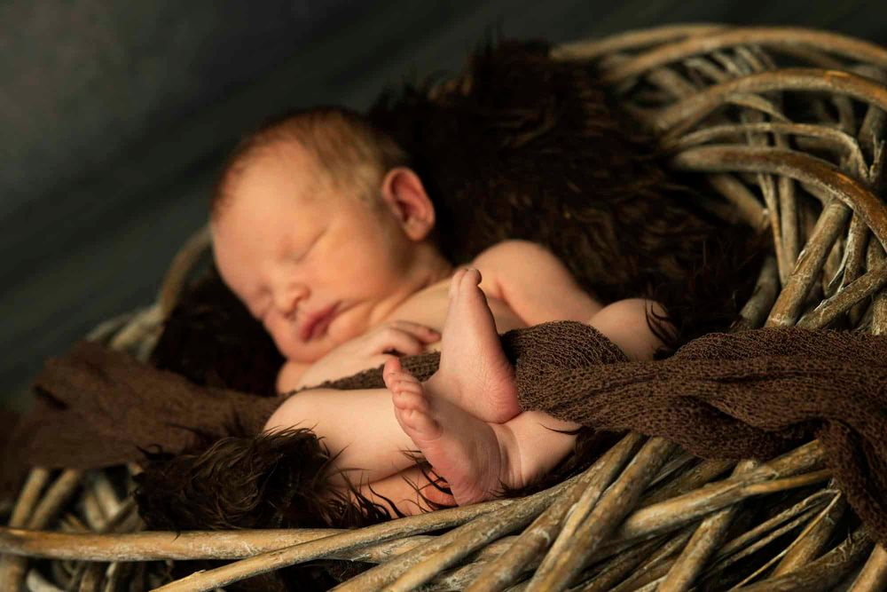 Nyfødt baby i kurv med føtter foran seg i fotostudio hos fotograf i Lyngdal