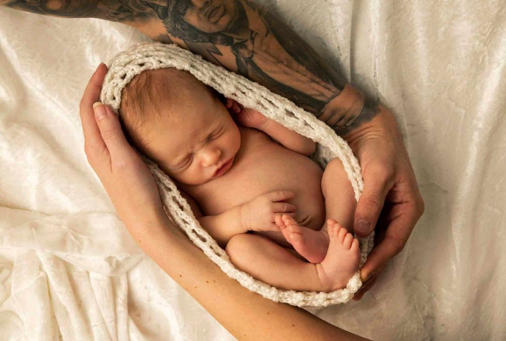 Nyfødt baby ligger sovende med mors og fars armer rundt seg på nyfødtfoto i Farsund
