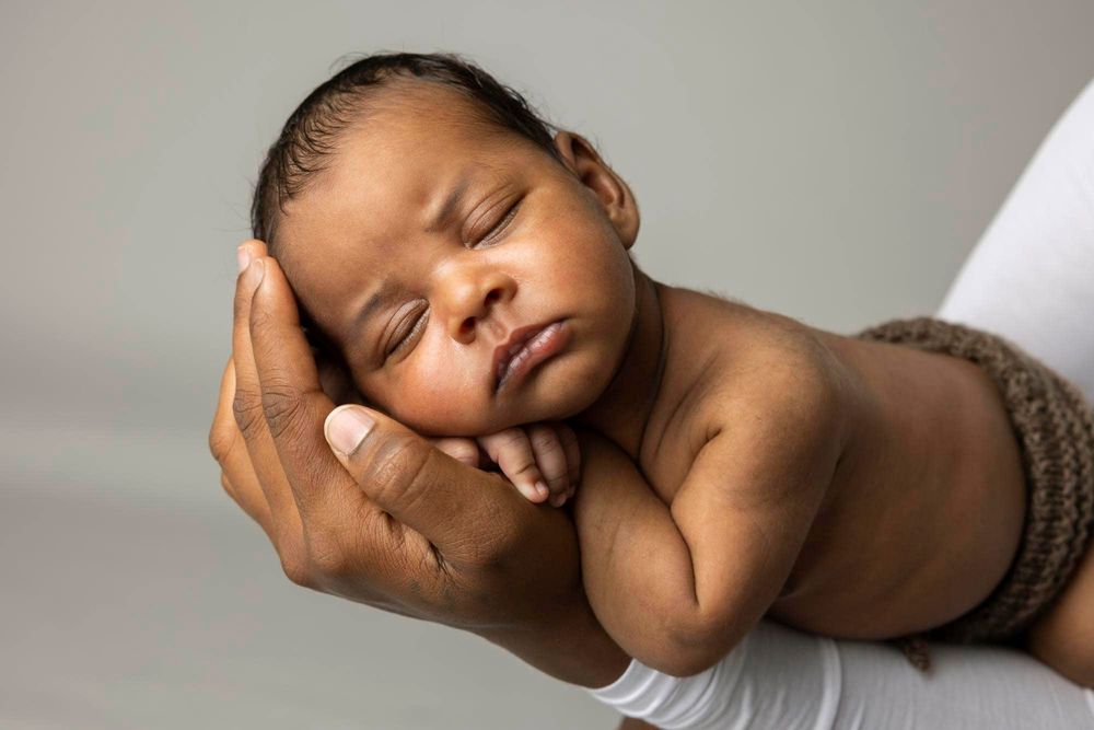 Mørk nyfødt baby som sover på magen i mors hender på nyfødtfotografering hos fotograf i Mandal