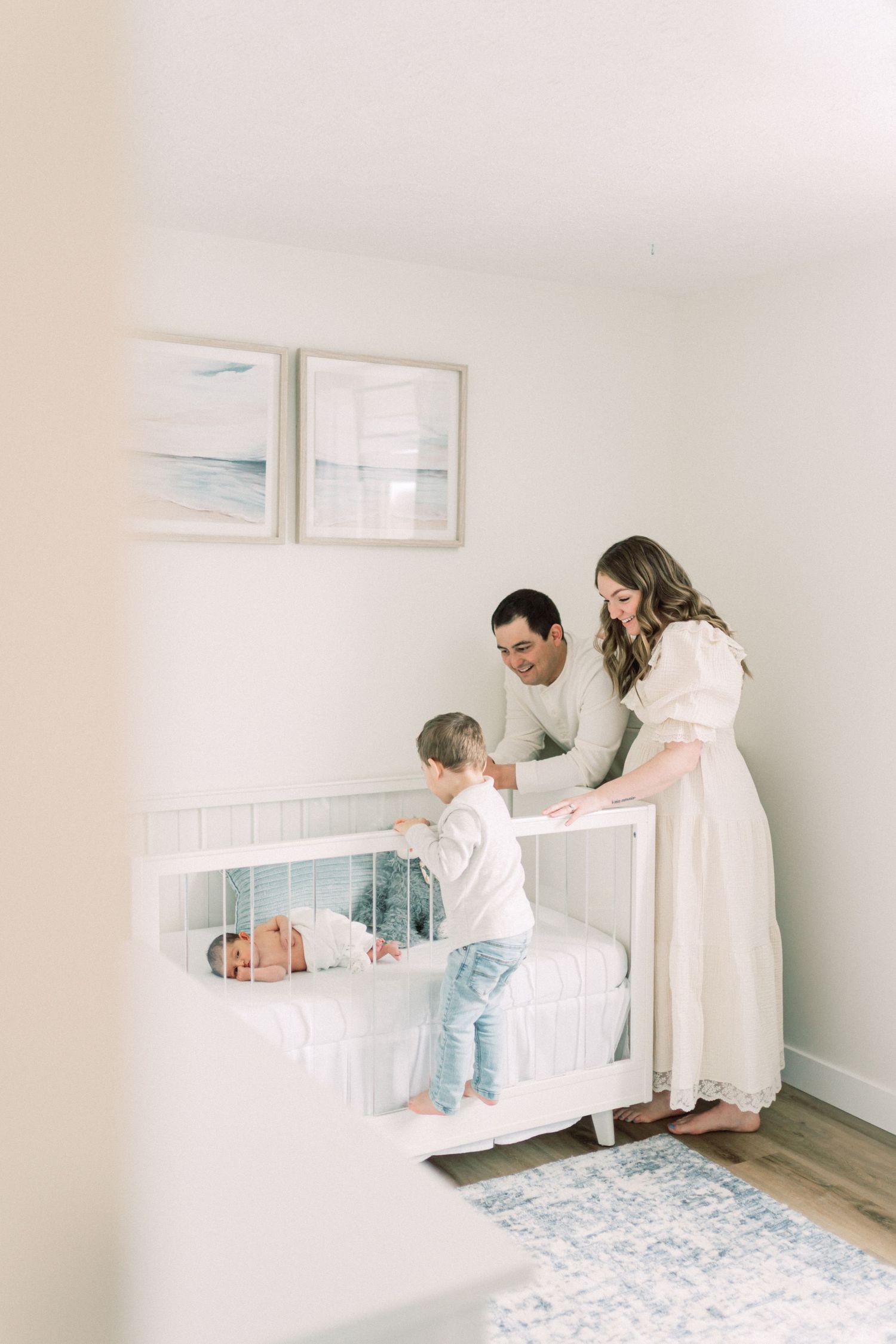 Family spends tender moment together in white nursery with decorative art and blue patterned rug.