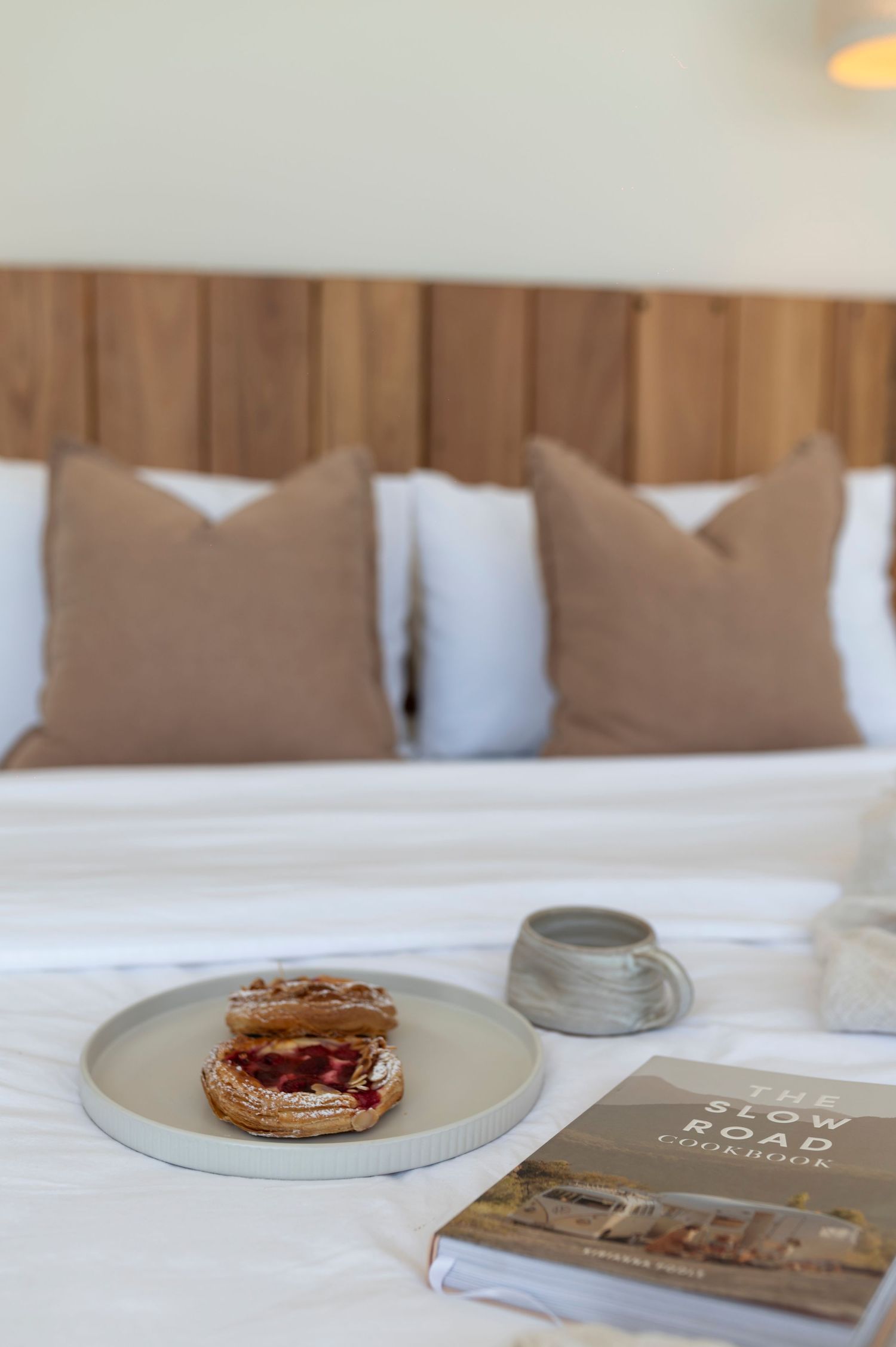 A cozy breakfast scene with toast on a ceramic plate, coffee cup, and book on crisp white hotel bedding.