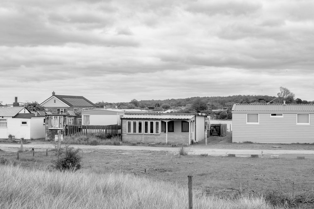 Black and white photo of small mobile homes and trailer residences arranged along a grassy coastal landscape.