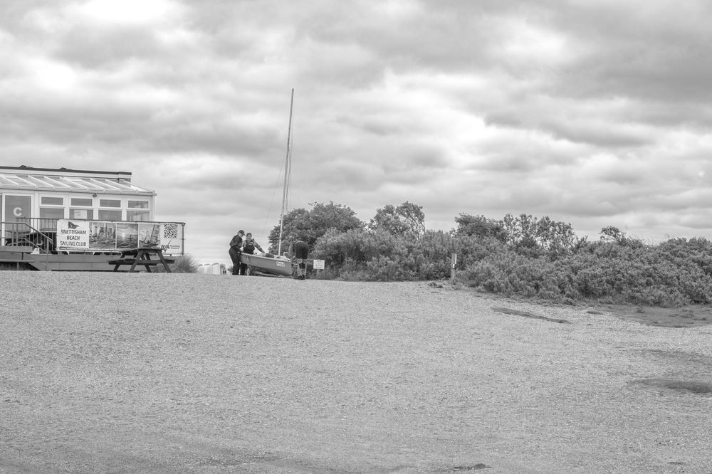 Black and white photo of a small rural building with vehicles parked outside under cloudy skies.