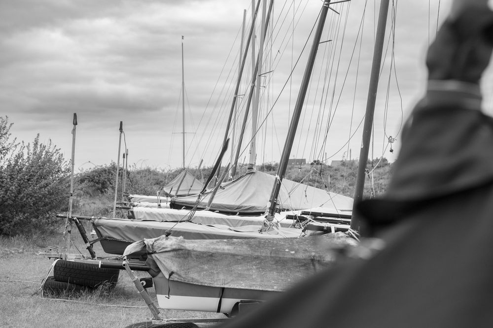 Black and white photograph of sailboats moored along a shoreline on an overcast day.