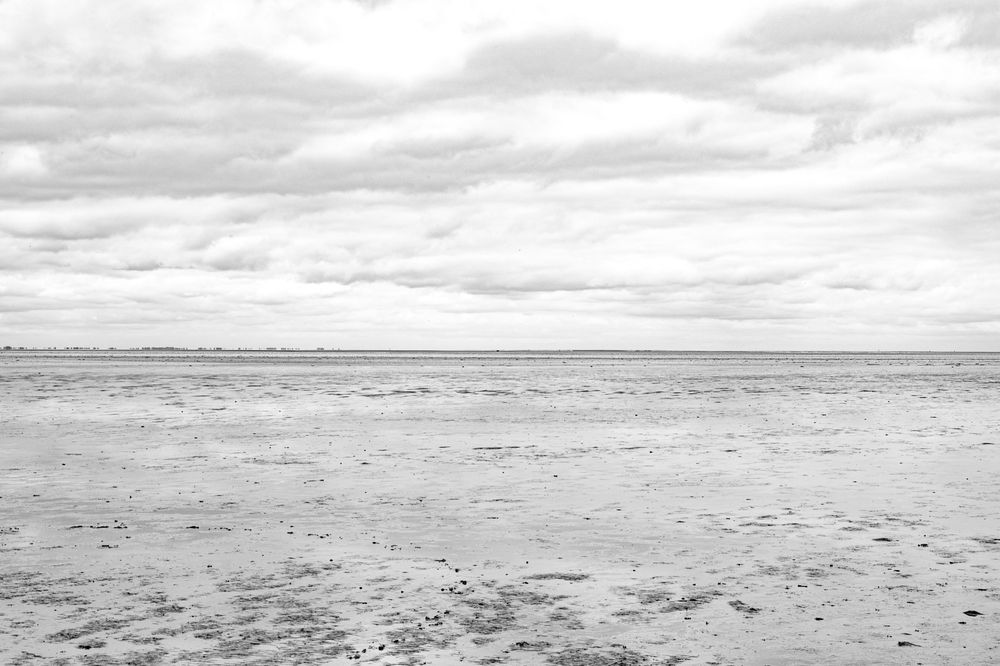 Minimalist black and white seascape showing an empty beach under cloudy skies.