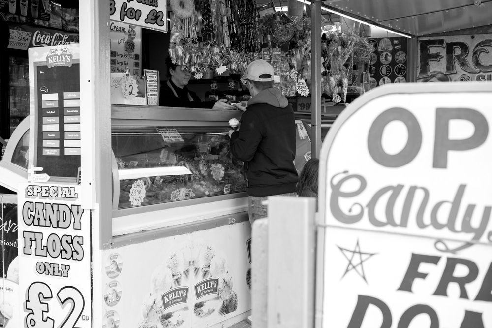 Black and white image of a carnival food stand with signs advertising cotton candy and other treats.