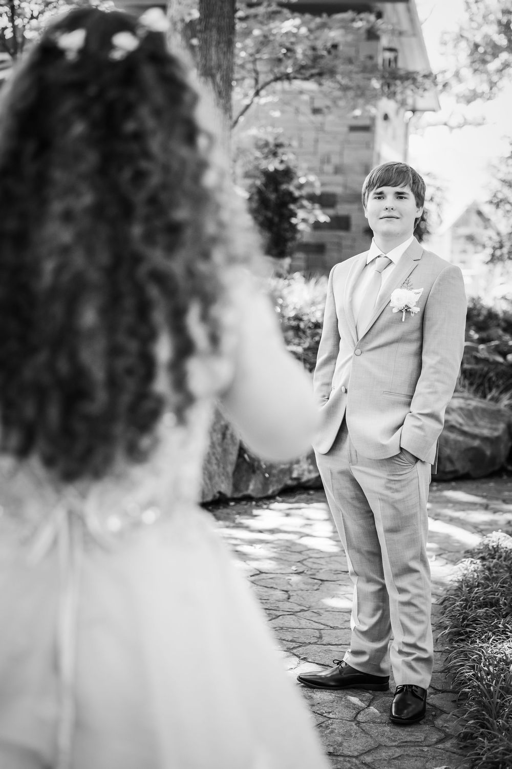 A black and white wedding photo capturing a first look moment between the groom in light suit and his bride on garden path.