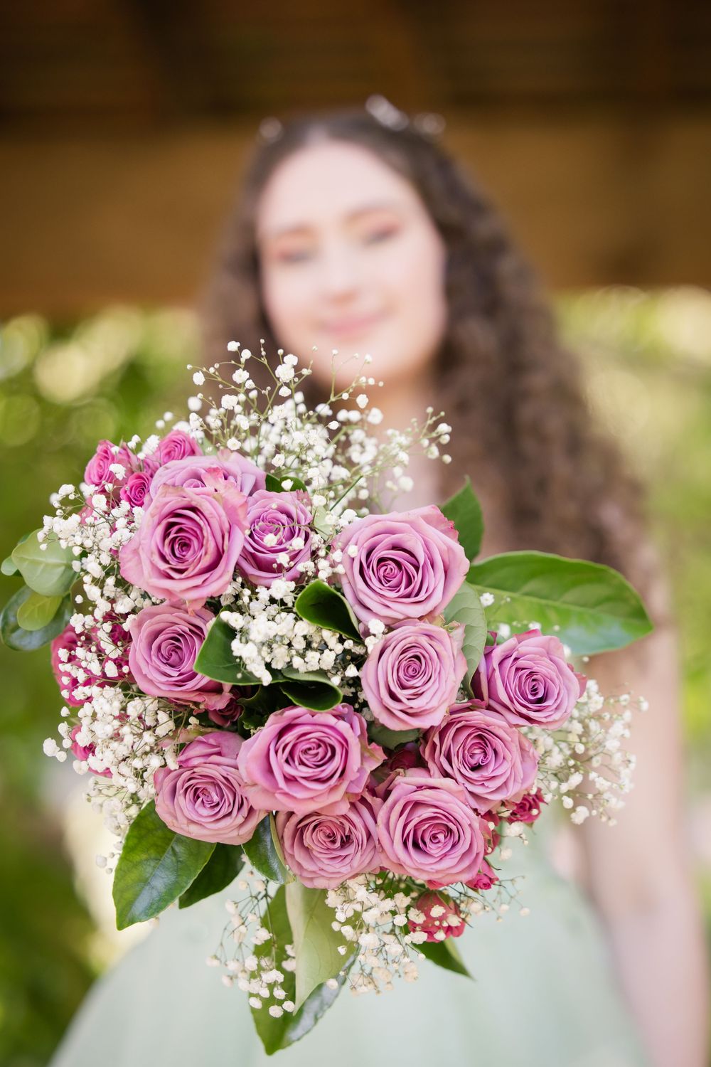 A beautiful bridal bouquet featuring pink roses and baby's breath against a soft blurred natural background.