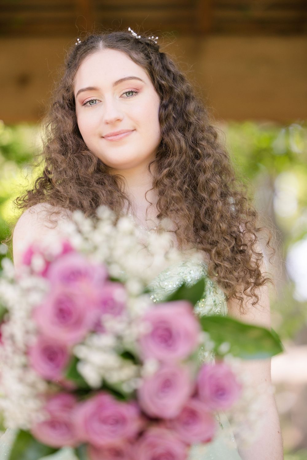 Beautiful portrait with long curly dark hair and pink roses in soft natural lighting outdoors.